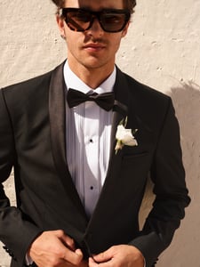 Ein Bräutigam in einem schicken schwarzen Anzug und lässiger Pose. Er trägt eine Sonnenbrille.