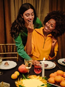 Auf dem Bild sind zwei Frauen zu sehen, die an einem gedeckten Tisch stehen und Snacks essen.