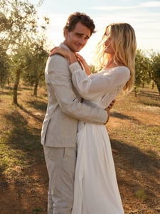 A groom and a bride embracing each other. The groom is wearing a boho suit and the bride a boho wedding dress.