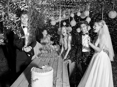 Eine Hochzeitsfeier, bei der der Best Man eine Champagne-Flasche vor dem Brautpaar und den Gästen öffnet.