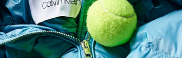 Blaue Daunenjacke von Calvin Klein, auf der ein Tennisball liegt