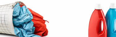 Ein umgefallener Wäschekorb mit roten und blauen Jacken und zwei verschiedenen Waschmittelflaschen