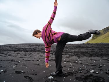 Balancerende man op een zwart strand met een fel gekleurde trui