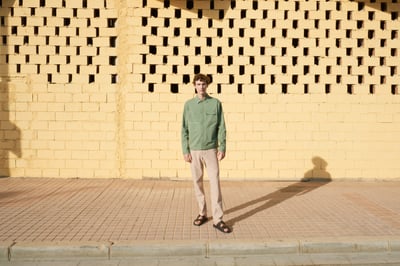 A man wearing a green jacket standing in front of a yellow wall