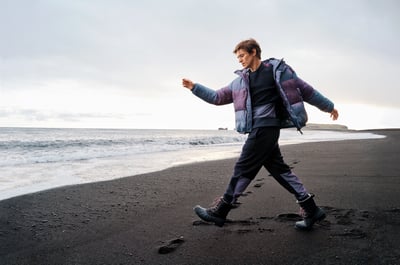 Man draagt een puffer jacket en loopt op een zwart strand