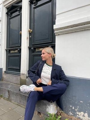 Nynke Camps sitting on the stairs at the front door while wearing a blue blazer, a white T-shirt, blue pants and white Sneakers